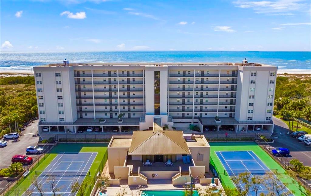 An aerial view of a multi-story beachfront condominium building with tennis courts and a pool — 420 BEACH ROAD UNIT 606, SARASOTA, FL