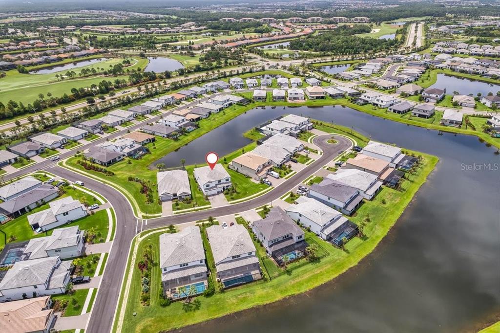 An aerial view shows a suburban neighborhood with houses surrounding a central pond — 5609 CLEARWATER COURT, LAKEWOOD RANCH, FL