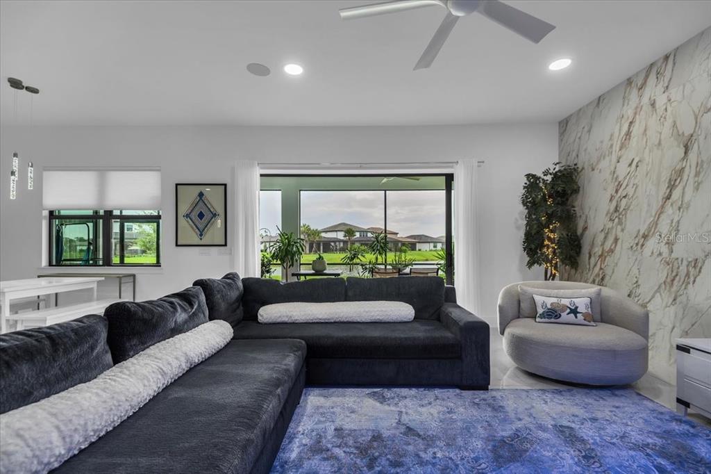 A living room features a large dark sectional, a round chair, and a marble accent wall — 5609 CLEARWATER COURT, LAKEWOOD RANCH, FL
