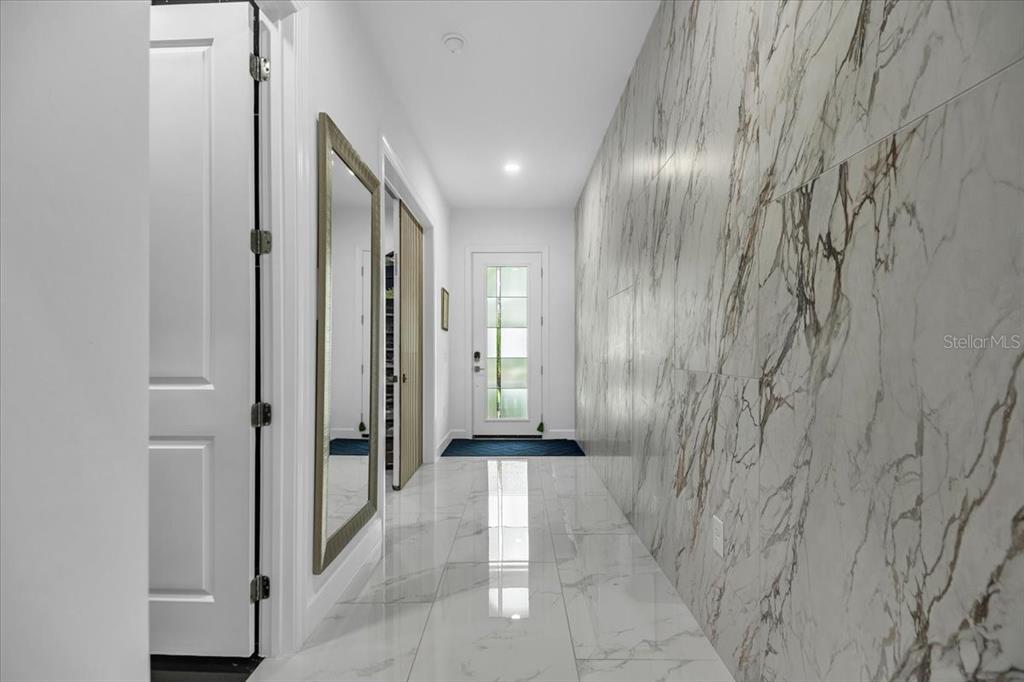 A hallway features white marble-look tile flooring, a large wall mirror, and marble-patterned wall tiles — 5609 CLEARWATER COURT, LAKEWOOD RANCH, FL