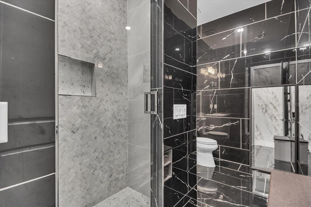A modern bathroom features a glass-enclosed shower with herringbone tile and black marble walls — 5609 CLEARWATER COURT, LAKEWOOD RANCH, FL