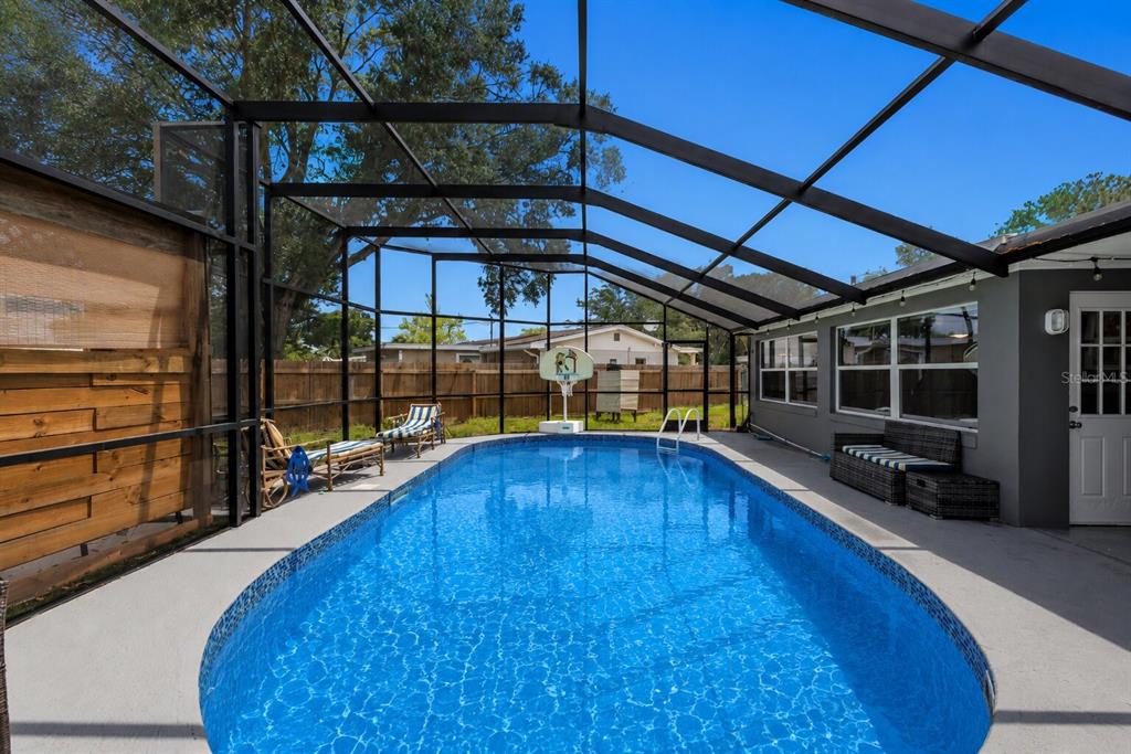 A screened-in swimming pool with a basketball hoop and patio furniture in a backyard — 6545 JACKSON STREET, NEW PORT RICHEY, FL