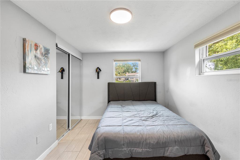 A bedroom features a bed with a grey comforter, mirrored closet doors, and tile flooring — 6545 JACKSON STREET, NEW PORT RICHEY, FL