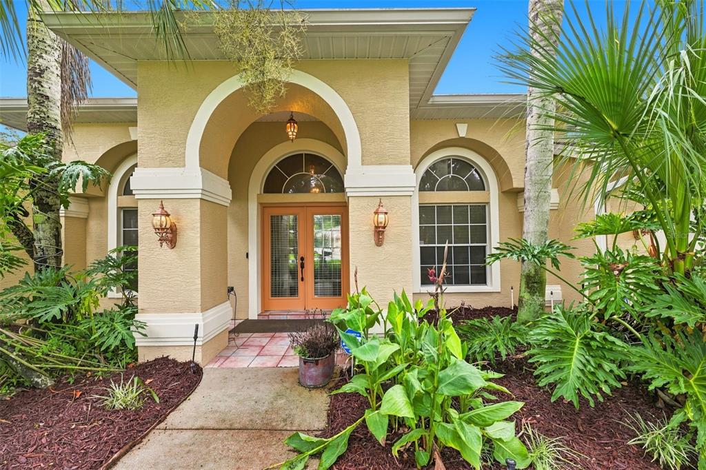The exterior of a tan house features a covered arched entryway with double glass doors — 18416 AUTUMN LAKE BOULEVARD, HUDSON, FL