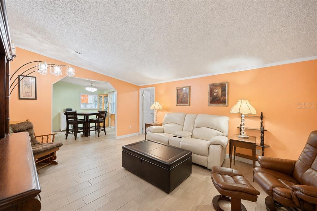 A living room with orange walls, light wood-look tile flooring, and a white leather sofa — 117 GLENN ROAD, AUBURNDALE, FL
