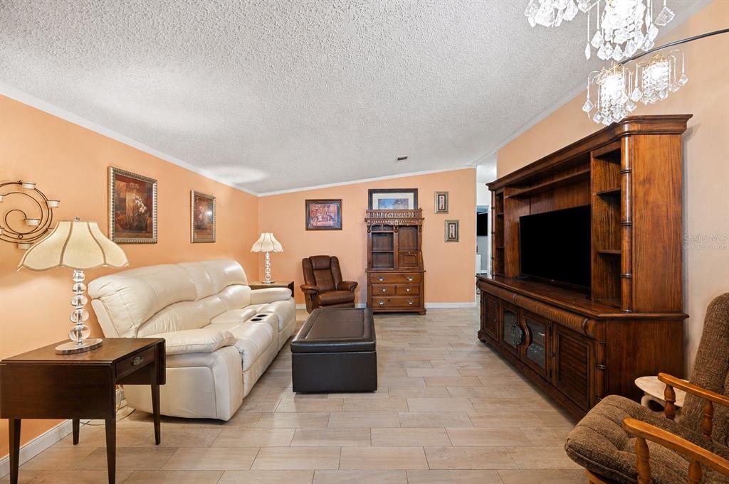 A living room features peach walls, tile flooring, a white sofa, and a large wooden entertainment center — 117 GLENN ROAD, AUBURNDALE, FL