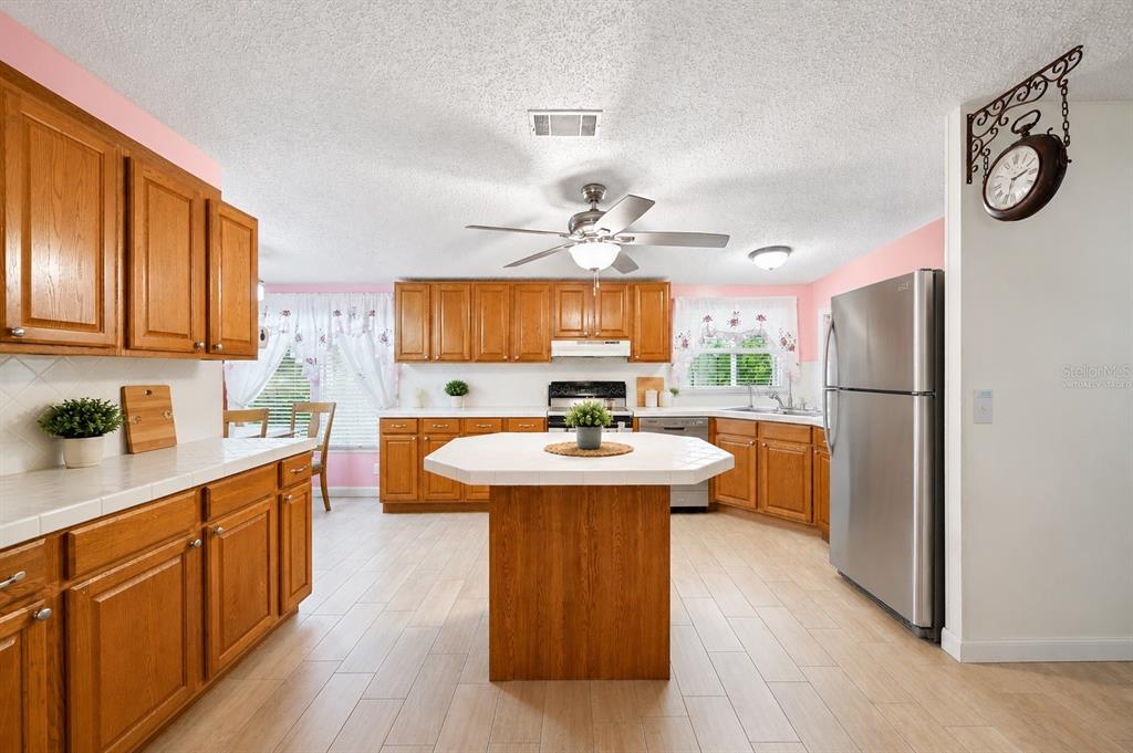A kitchen with wood cabinets, a tiled island, stainless steel appliances, and light-colored flooring — 117 GLENN ROAD, AUBURNDALE, FL