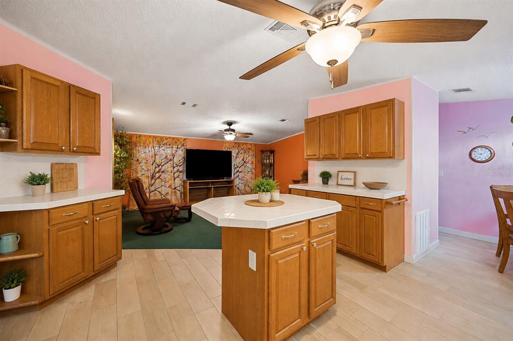 A kitchen with oak cabinets and a tiled island opens into a living area — 117 GLENN ROAD, AUBURNDALE, FL