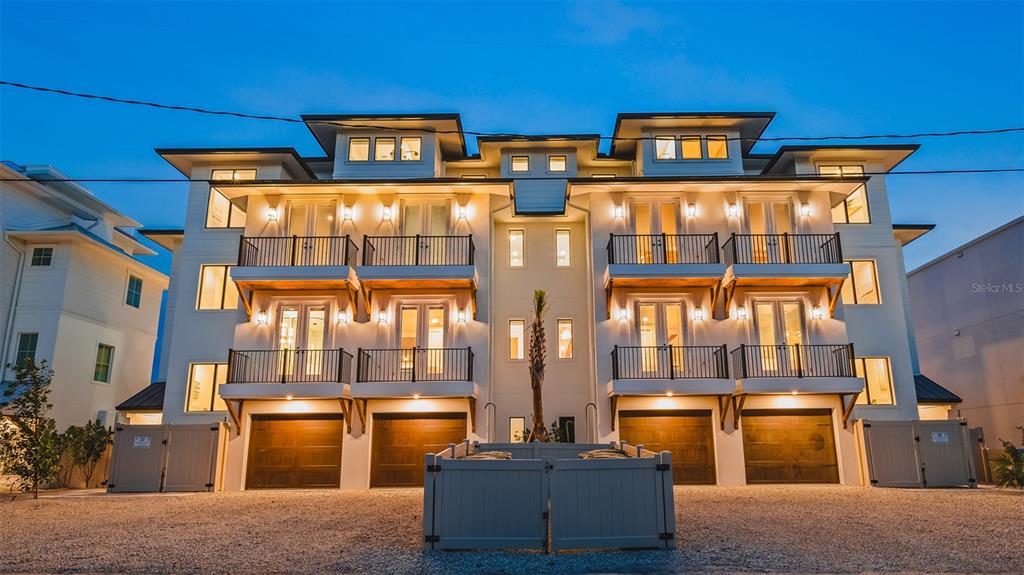 A multi-story residential building with four garage doors, balconies, and exterior lighting at dusk — 1142 WINDSONG LANE UNIT A, SARASOTA, FL