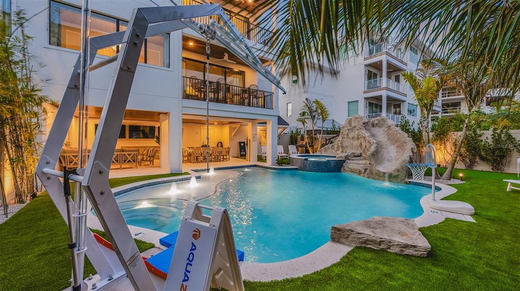 A backyard features a swimming pool with a rock slide, hot tub, and patio area — 1142 WINDSONG LANE UNIT A, SARASOTA, FL