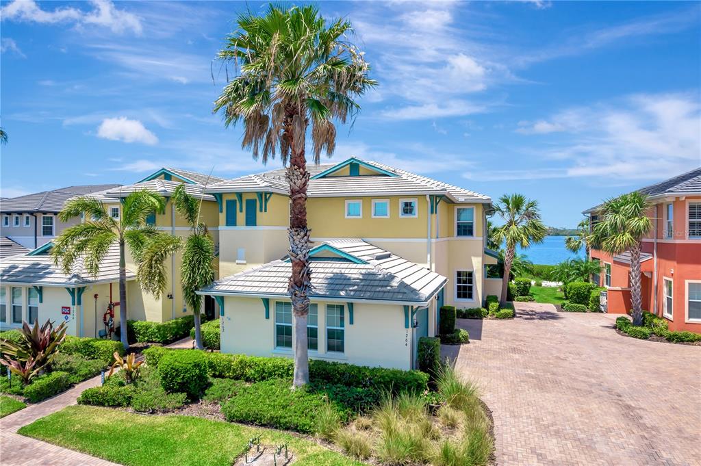 An exterior view of a multi-story yellow townhouse with a palm tree and water view — 1264 RIVERSCAPE STREET UNIT B, BRADENTON, FL