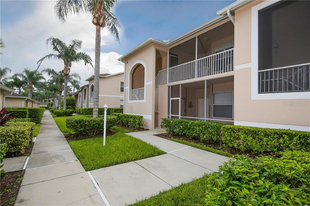 A two-story apartment building features beige stucco walls, screened-in balconies, and a concrete walkway — 5330 HYLAND HILLS AVENUE UNIT 2321, SARASOTA, FL