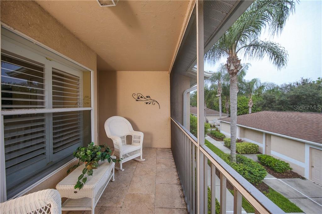 A screened-in balcony features tile flooring, white wicker furniture, and a view of palm trees — 5330 HYLAND HILLS AVENUE UNIT 2321, SARASOTA, FL