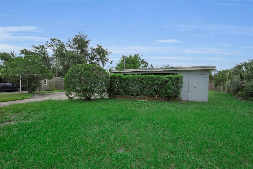 A grassy yard features a small, gray detached building with a hedge-lined carport — 509 BROXBURN AVENUE, TAMPA, FL