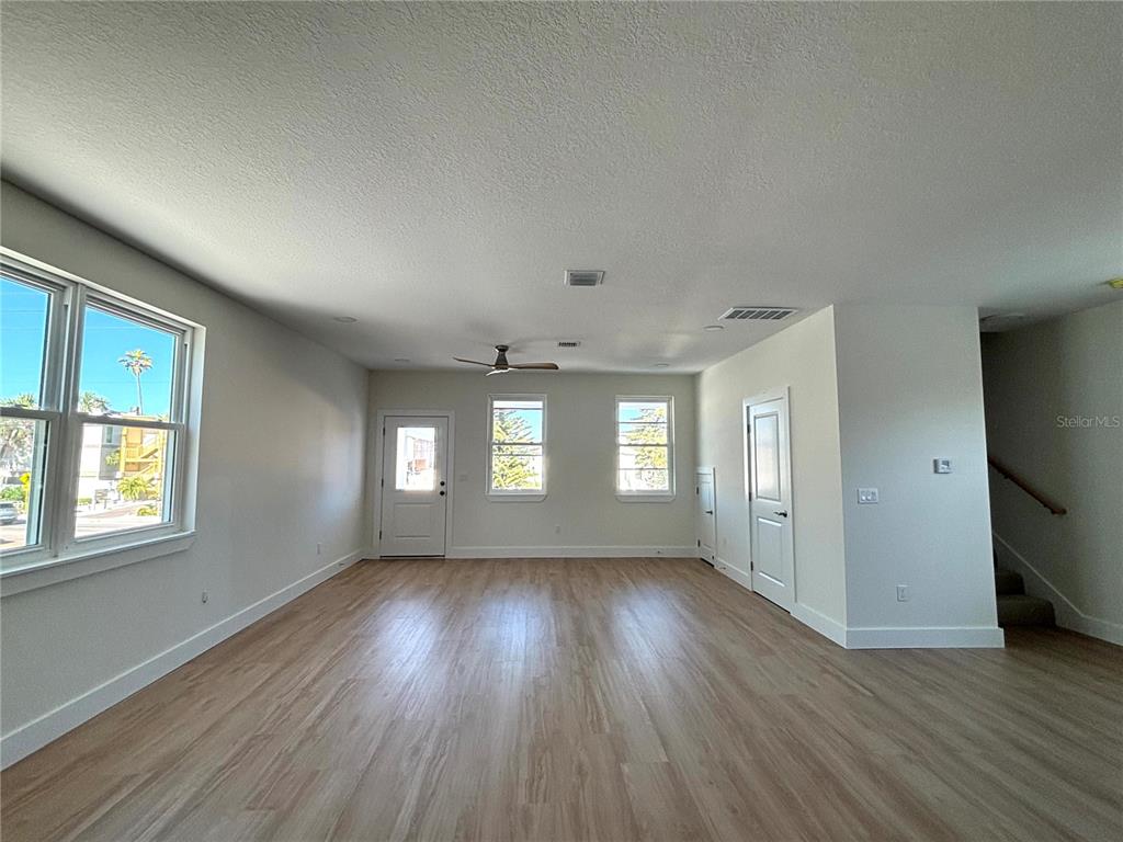 An empty room features light wood-look flooring, white walls, a ceiling fan, and multiple windows — 711 GULF BOULEVARD, INDIAN ROCKS BEACH, FL
