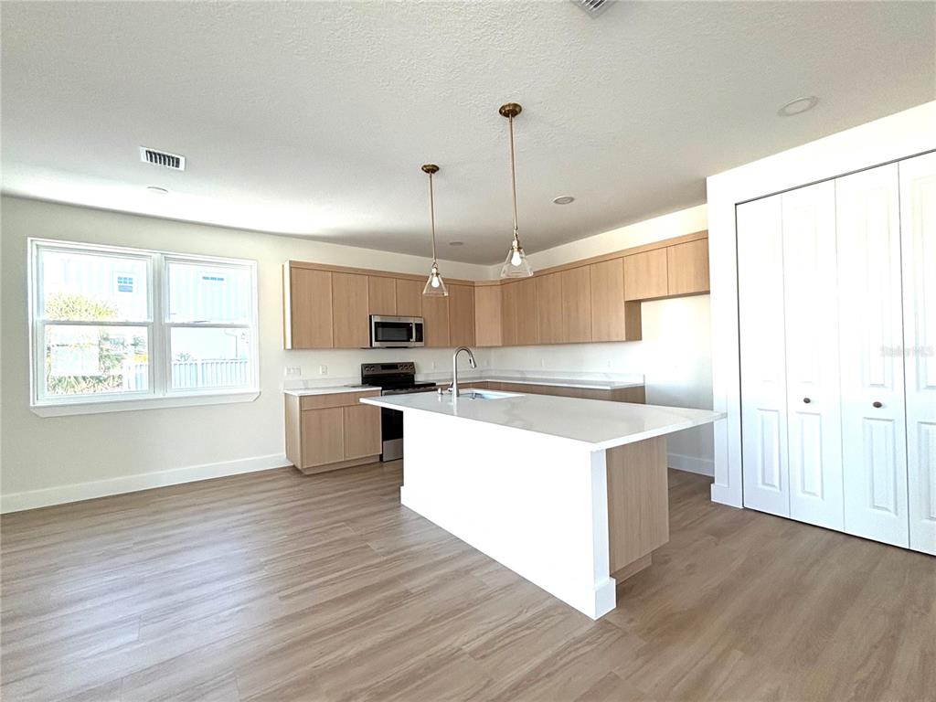 A modern kitchen features light wood cabinets, a white island, and light-colored wood-look flooring — 711 GULF BOULEVARD, INDIAN ROCKS BEACH, FL