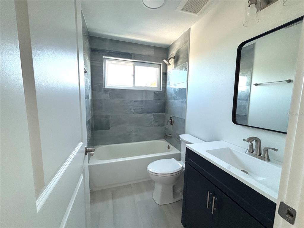 A bathroom features a dark vanity, a mirror, a toilet, and a tub with tiled walls — 711 GULF BOULEVARD, INDIAN ROCKS BEACH, FL
