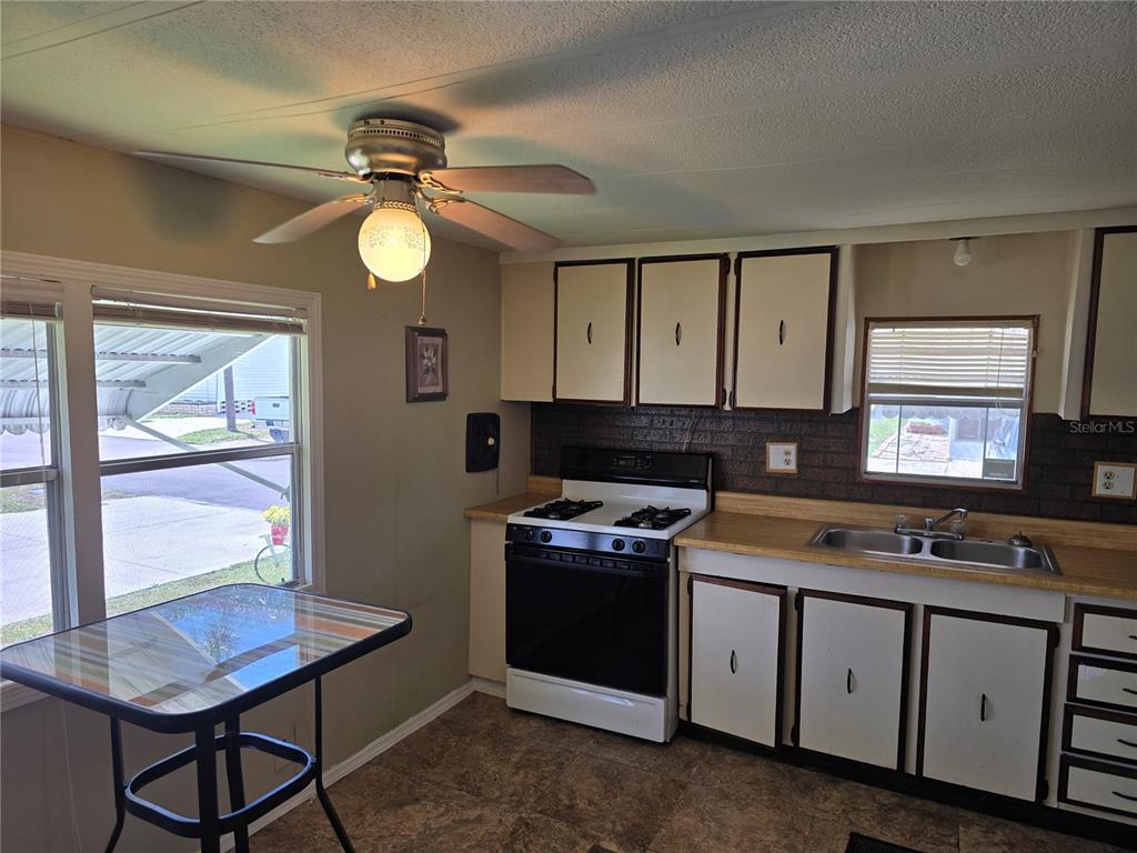 A kitchen features white cabinets with dark trim, a gas stove, and a small dining table — 5316 53RD AVENUE E UNIT A21, BRADENTON, FL