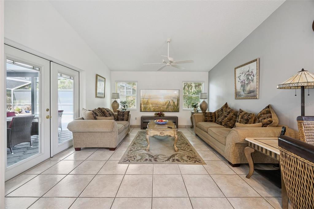 A living room with tile flooring, two beige sofas, a coffee table, and glass doors — 2948 PEMBRIDGE STREET, KISSIMMEE, FL