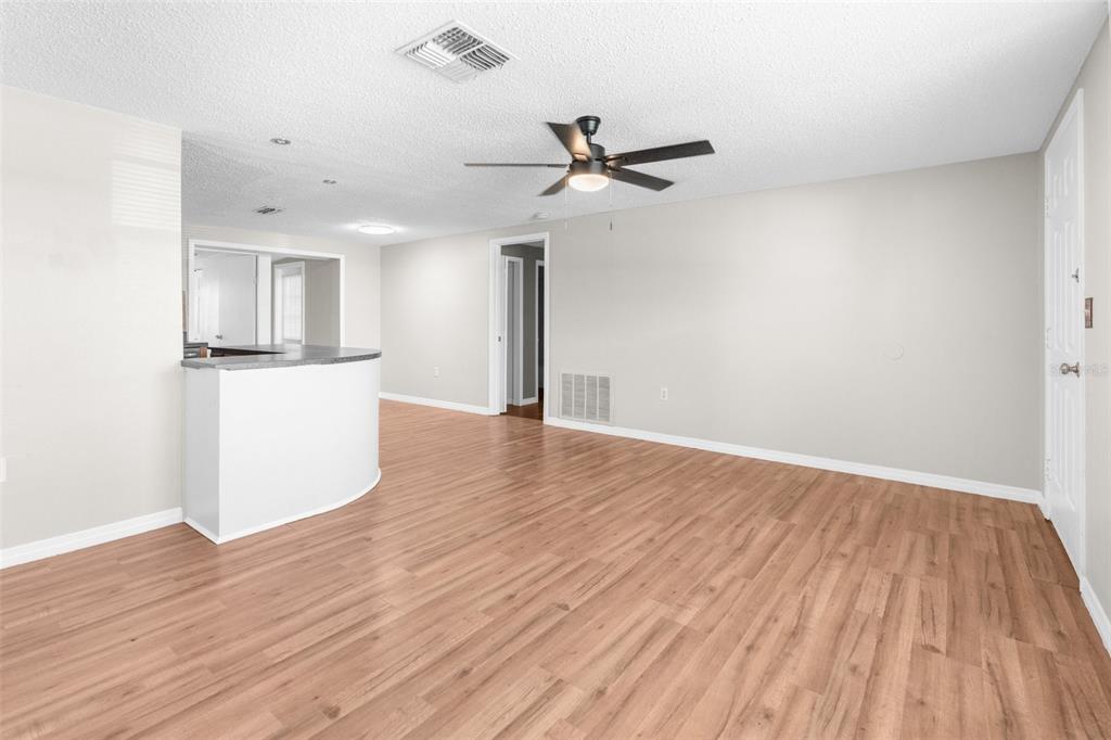 An empty living room with light wood-look flooring, a ceiling fan, and a kitchen counter — 11902 OCEANSIDE DRIVE, PORT RICHEY, FL