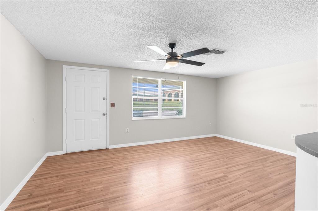 An empty room with light wood-look flooring, a ceiling fan, and a white entry door — 11902 OCEANSIDE DRIVE, PORT RICHEY, FL