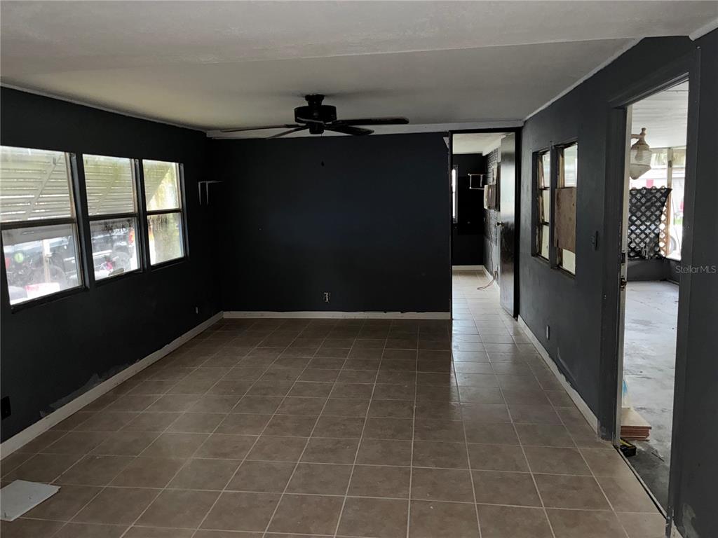 An empty room features dark gray walls, tiled flooring, a ceiling fan, and multiple windows — 25 SUNSET CIRCLE, LAKE ALFRED, FL
