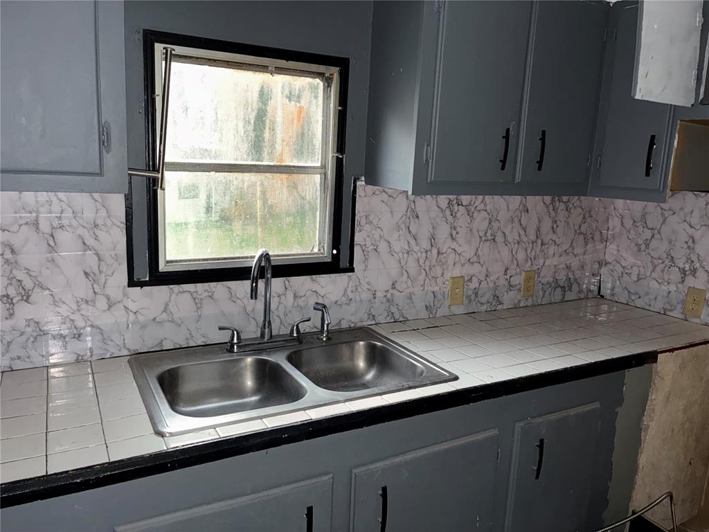 A kitchen features gray cabinets, a double-basin sink, and marble-patterned backsplash tiles — 25 SUNSET CIRCLE, LAKE ALFRED, FL