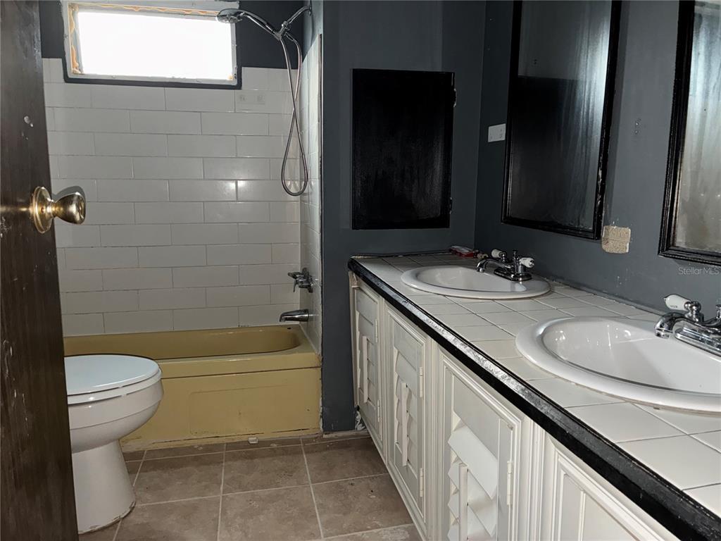 A bathroom features a yellow bathtub, a double vanity with tiled counters, and dark walls — 25 SUNSET CIRCLE, LAKE ALFRED, FL