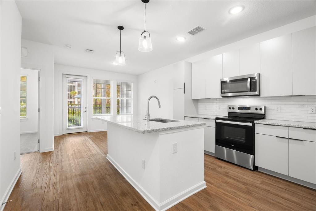 A modern kitchen features white cabinets, stainless steel appliances, a granite island, and wood flooring — 1700 RANCH ROAD UNIT A2-6108, NOKOMIS, FL