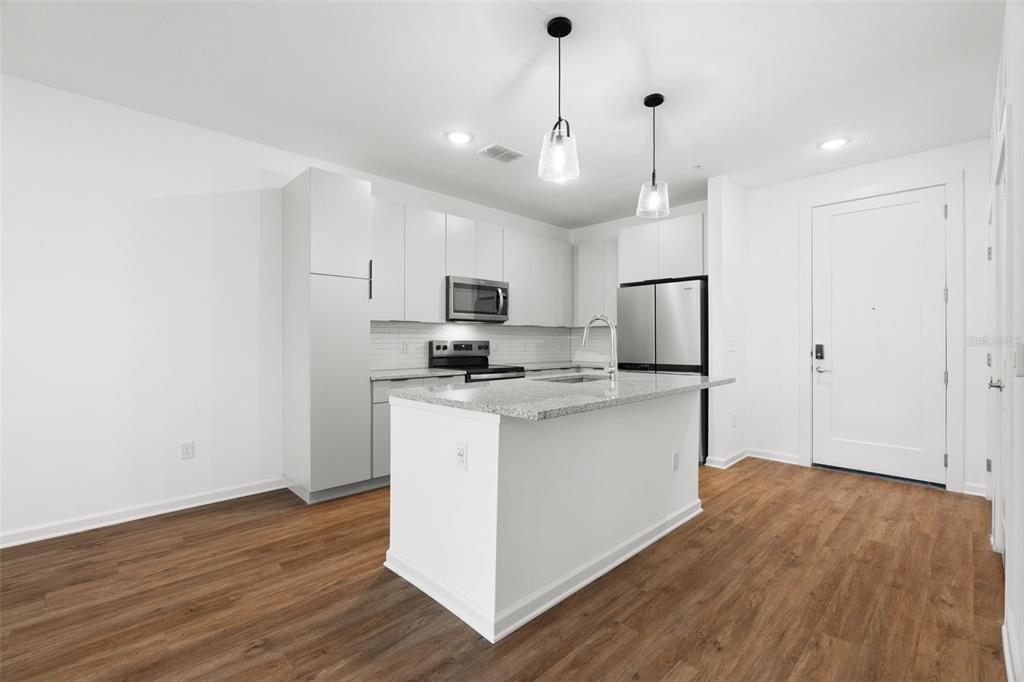 A modern kitchen features white cabinetry, stainless steel appliances, a granite island, and wood flooring — 1700 RANCH ROAD UNIT A2-6108, NOKOMIS, FL