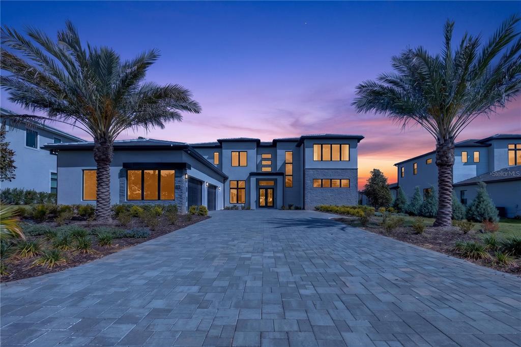 A two-story modern house with a paved driveway and palm trees at dusk — 16044 PENDIO DRIVE, BELLA COLLINA, FL