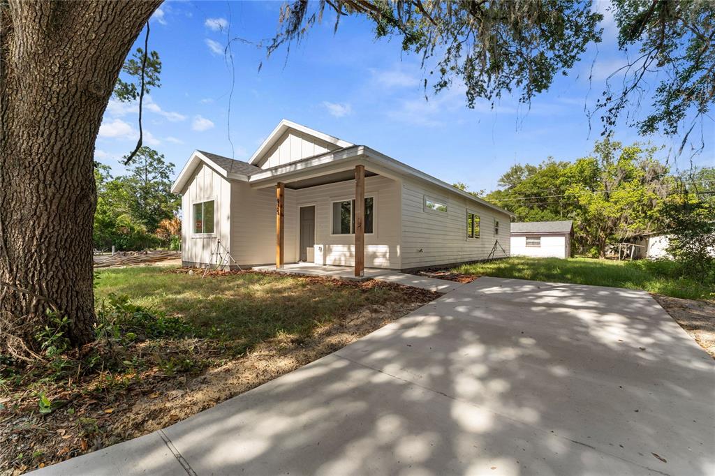 A single-story white house with a front porch and concrete driveway sits under large trees — 925 NE 17TH DRIVE, GAINESVILLE, FL