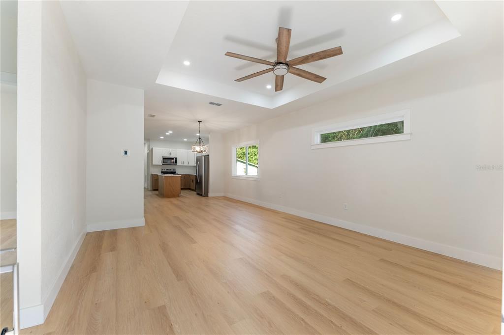 This open-concept living area features light wood flooring, a tray ceiling with a fan, and a kitchen — 925 NE 17TH DRIVE, GAINESVILLE, FL