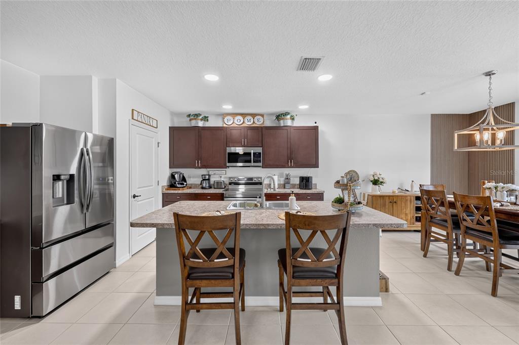 A kitchen features dark wood cabinets, a central island with two chairs, and stainless appliances — 4222 NE 29TH PLACE, OCALA, FL