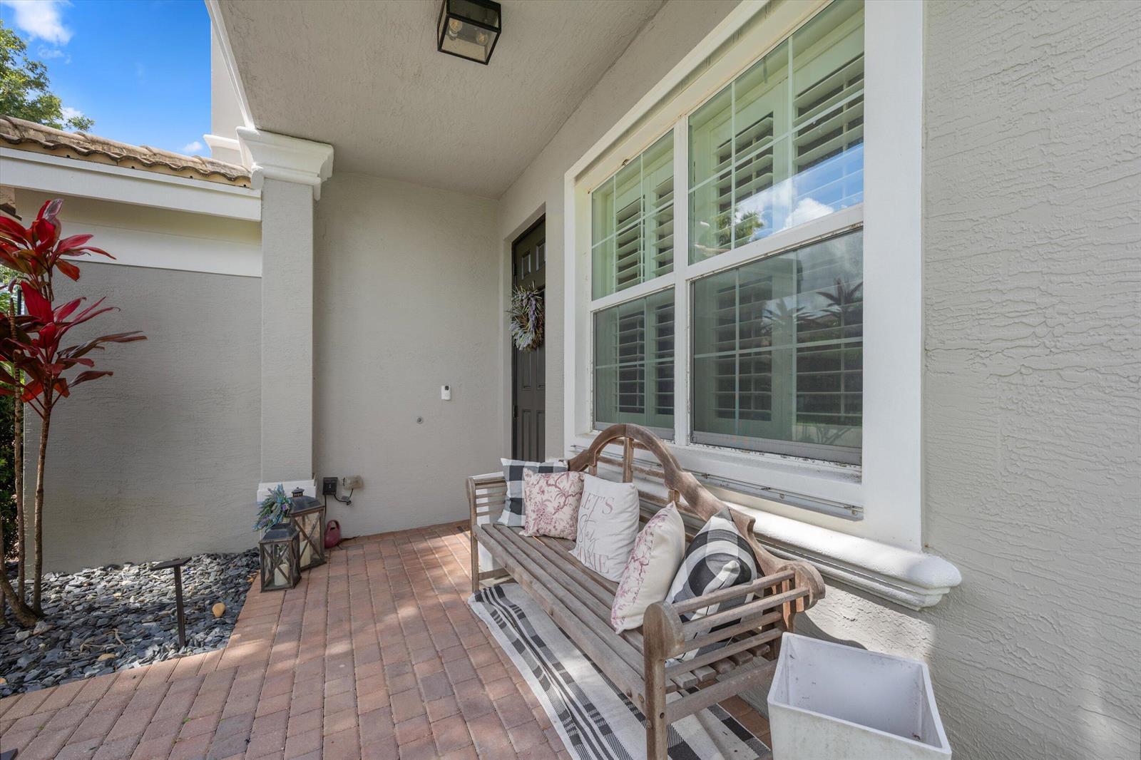 A covered front porch features a brick floor, a wooden bench, and a large window — 11577 Ponywalk Trail, Boynton Beach FL 33473, BOYNTON BEACH, FL