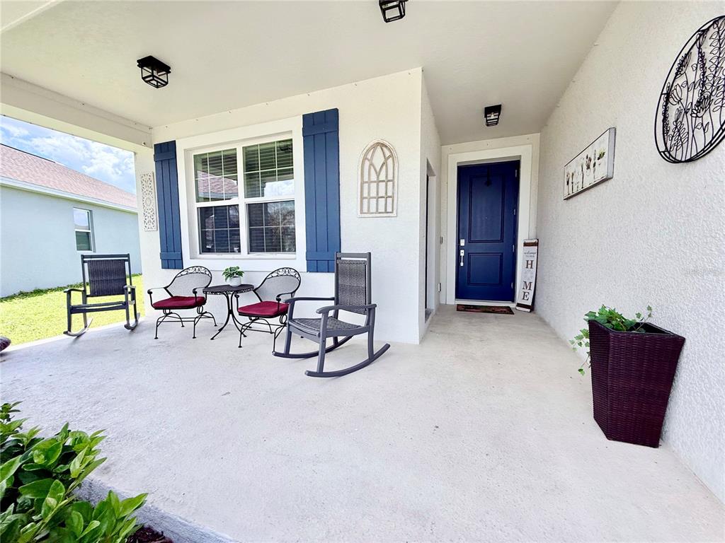 A covered front porch features a blue door, rocking chairs, and a small bistro set — 1578 CONTENTMENT LOOP, KISSIMMEE, FL