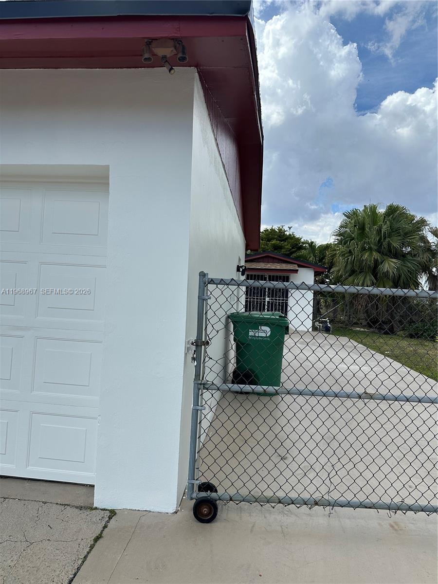 A white garage wall stands next to a chain-link fence and a green trash bin — 15200 SW 109 ave, Miami FL 33157, MIAMI, FL