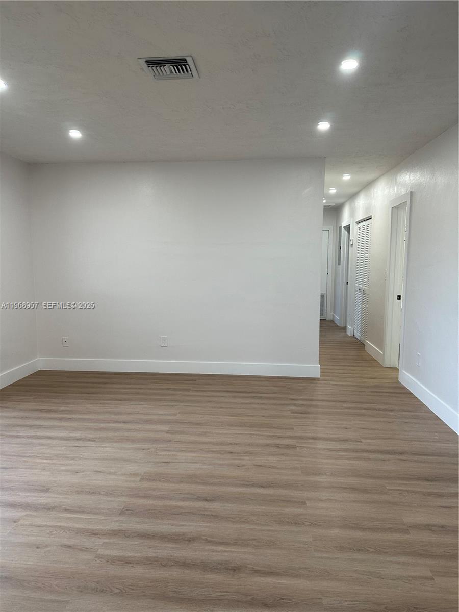 An empty room features light wood-look flooring, white walls, recessed lighting, and a hallway entrance — 15200 SW 109 ave, Miami FL 33157, MIAMI, FL