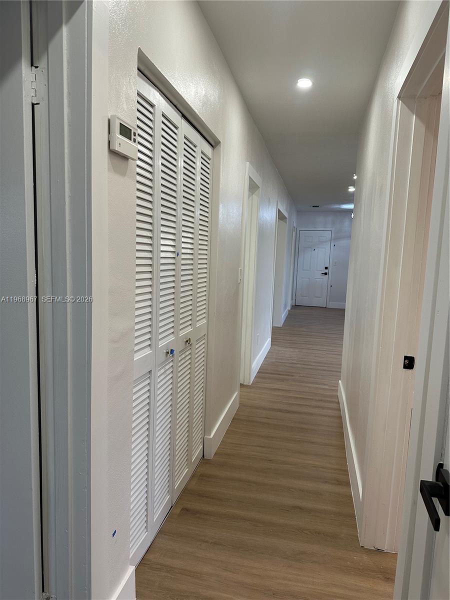 A hallway with light wood-look flooring leads to a white door in the distance — 15200 SW 109 ave, Miami FL 33157, MIAMI, FL