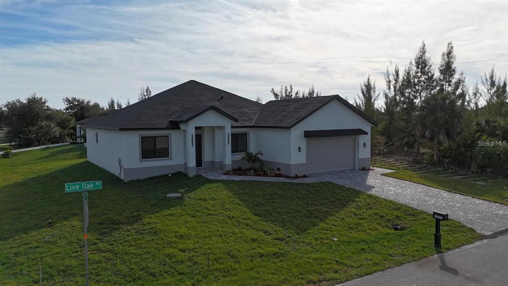 A single-story house with a white exterior, dark roof, and paved driveway sits on a lawn — 10426 LIVE OAK ROAD, PORT CHARLOTTE, FL