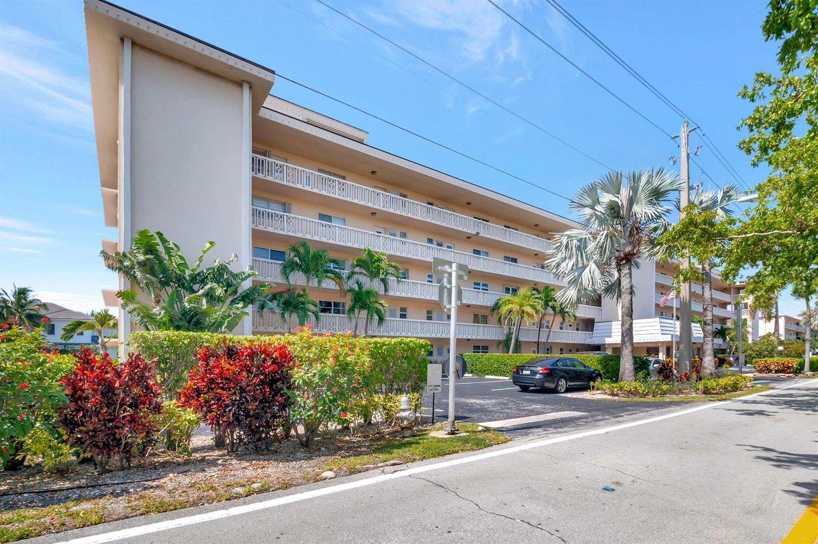 A multi-story apartment building features white balconies and a parking lot with palm trees — 750 NE Spanish River Boulevard # 103, Boca Raton FL 33431, BOCA RATON, FL