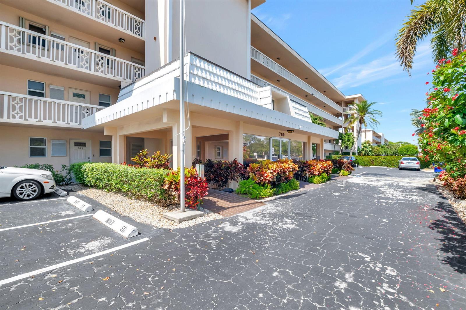 The exterior of a multi-story apartment building features a covered entrance and a parking lot — 750 NE Spanish River Boulevard # 103, Boca Raton FL 33431, BOCA RATON, FL