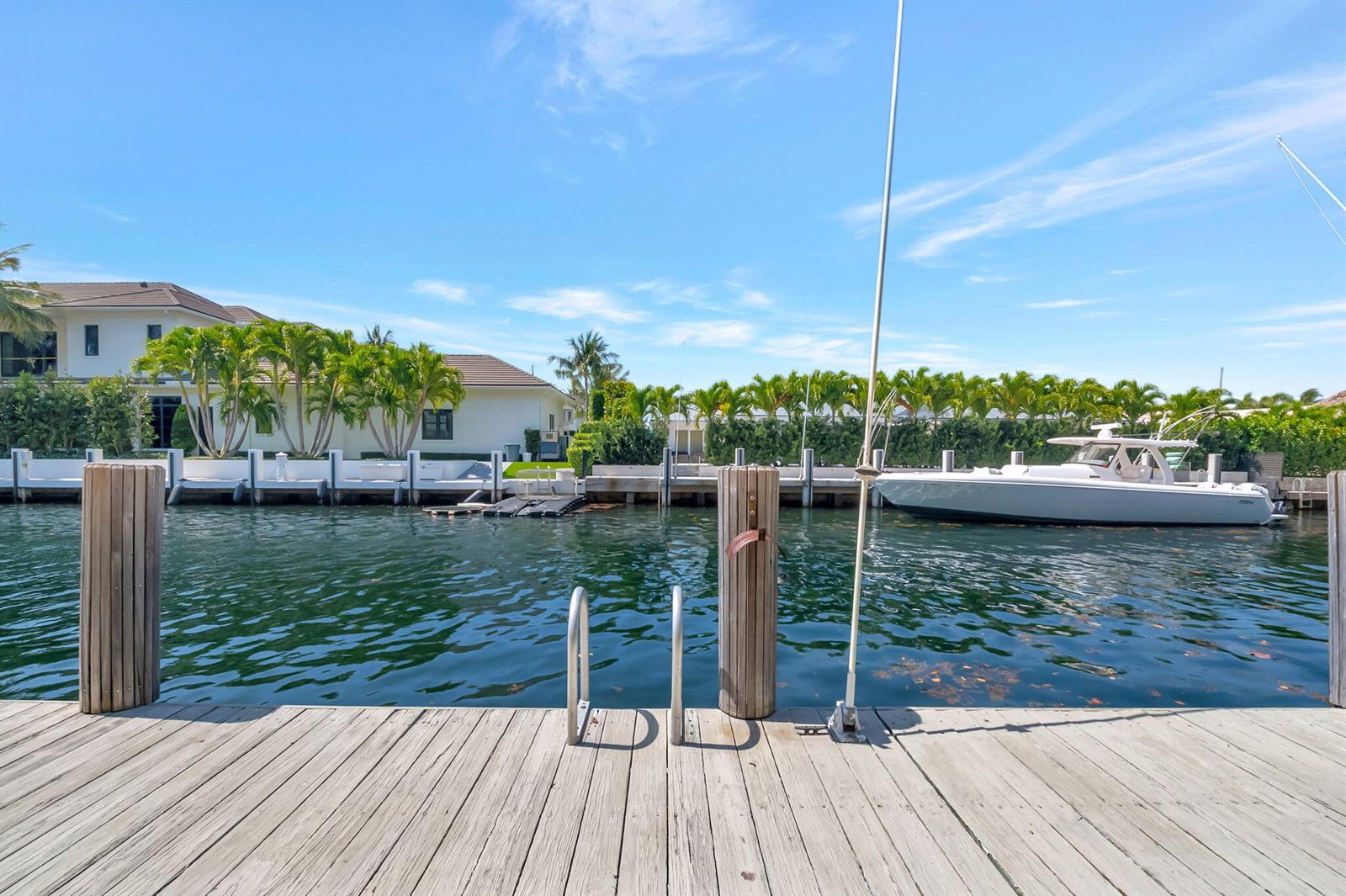 A wooden dock overlooks a canal with a boat and waterfront houses in the background — 750 NE Spanish River Boulevard # 103, Boca Raton FL 33431, BOCA RATON, FL