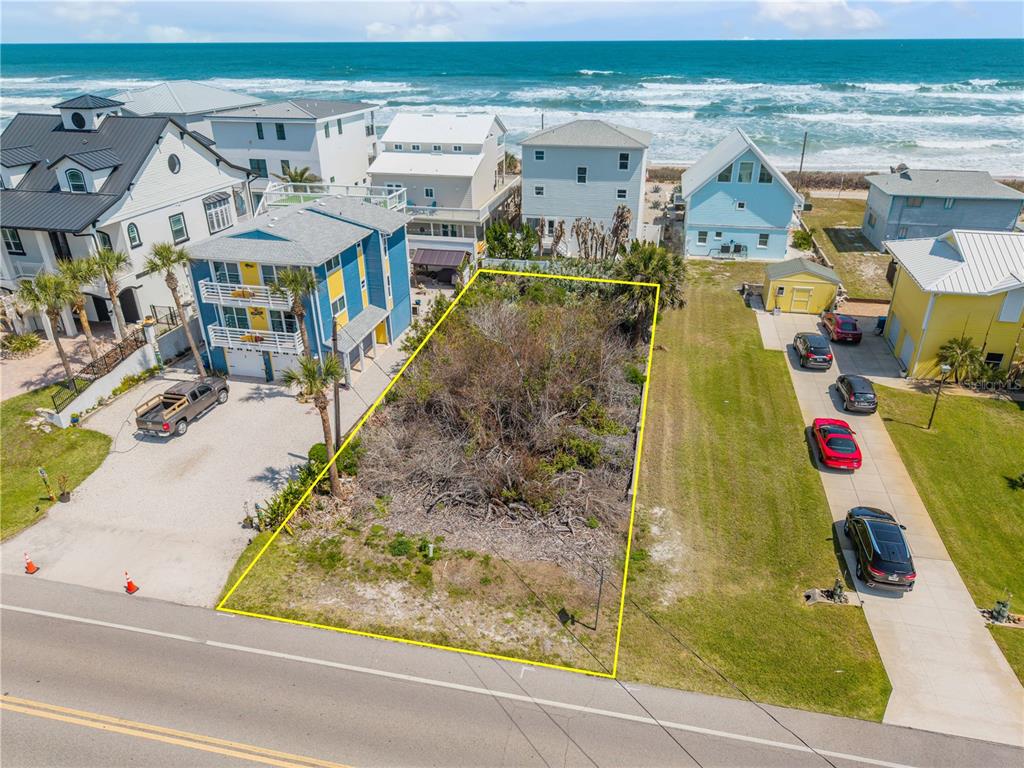 An aerial view shows a vacant, brush-covered rectangular lot situated between two houses near the ocean — TURTLEMOUND ROAD, NEW SMYRNA BEACH, FL