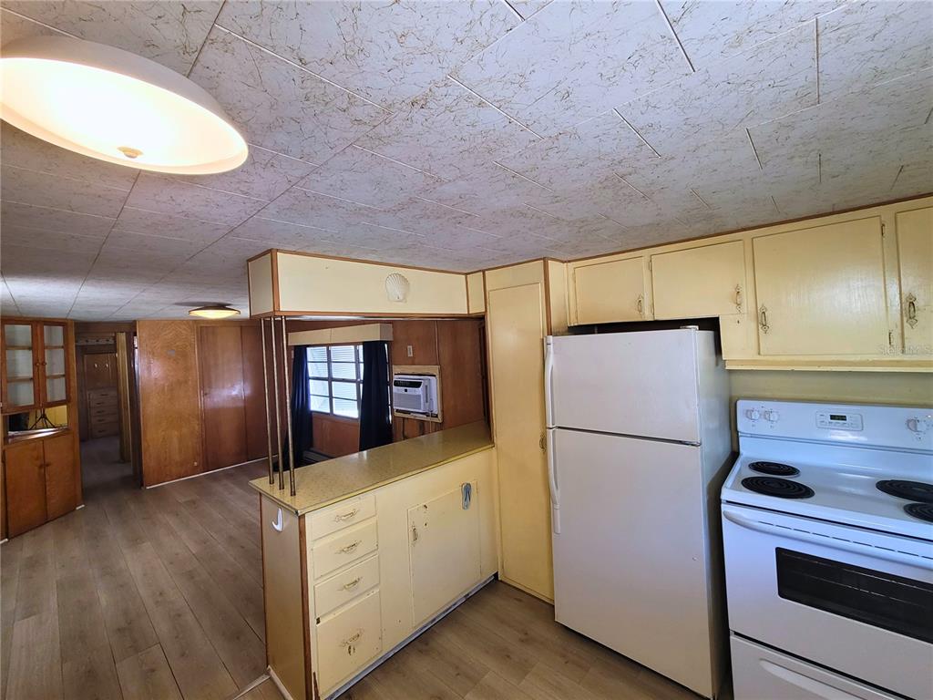 A kitchen with yellow cabinets, a white refrigerator, and a breakfast bar overlooking the living area — 522 49TH AVENUE W, BRADENTON, FL