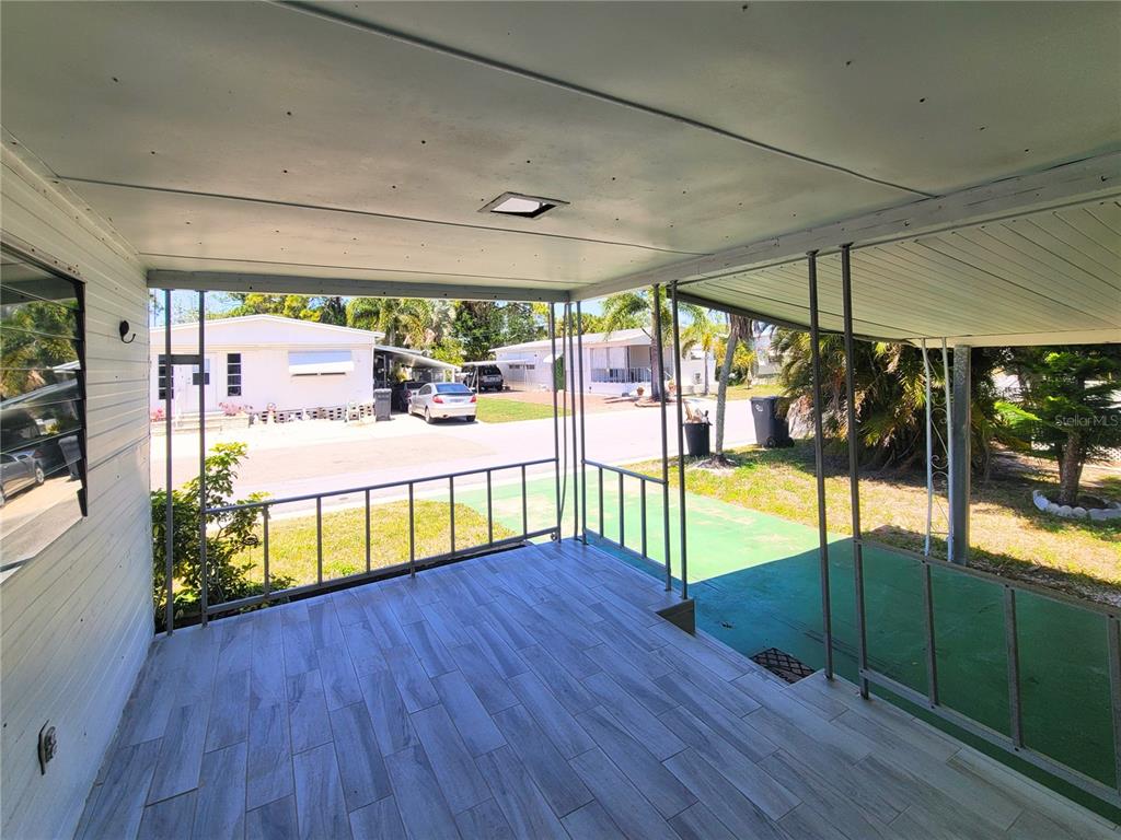 A covered outdoor porch features wood-look tile flooring and metal railings overlooking a residential street — 522 49TH AVENUE W, BRADENTON, FL