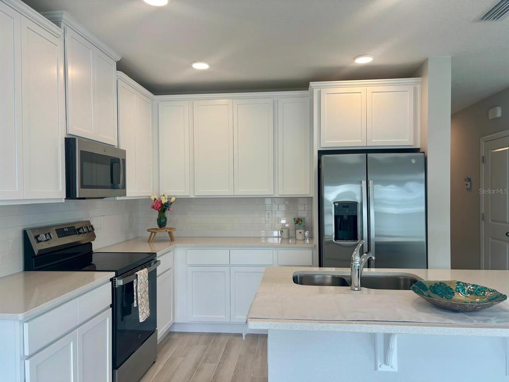 A kitchen features white cabinets, stainless steel appliances, a subway tile backsplash, and quartz countertops — 4616 CAMPSITE, ORLANDO, FL