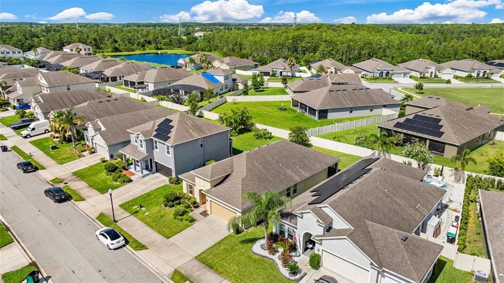 An aerial view shows suburban houses with solar panels and fenced backyards near a pond — 12216 PRAIRIE PLANTATION WAY, ORLANDO, FL