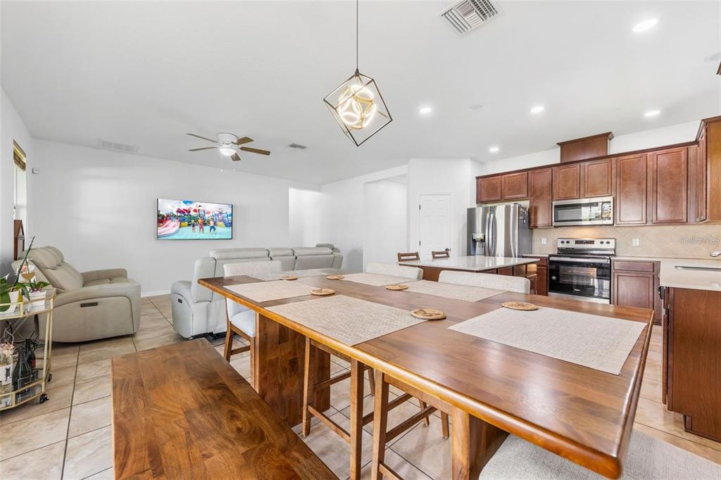 A dining area with a wooden table and bench sits adjacent to a kitchen and living room — 12216 PRAIRIE PLANTATION WAY, ORLANDO, FL
