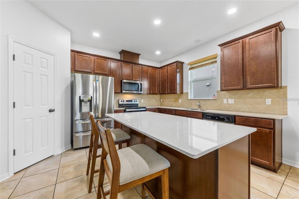 A kitchen features dark wood cabinets, stainless steel appliances, a white island, and tile flooring — 12216 PRAIRIE PLANTATION WAY, ORLANDO, FL